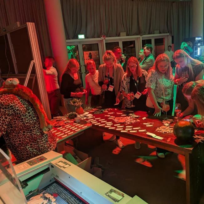 G&auml;ste w&auml;hlen bei einer Abendveranstaltung ihre Gravur, die Laserstation von LASERPIX arbeitet im Hintergrund